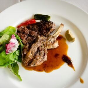 Exquisite lamb chop with sauce, greens and vegetables on a white plate, perfect for fine dining.