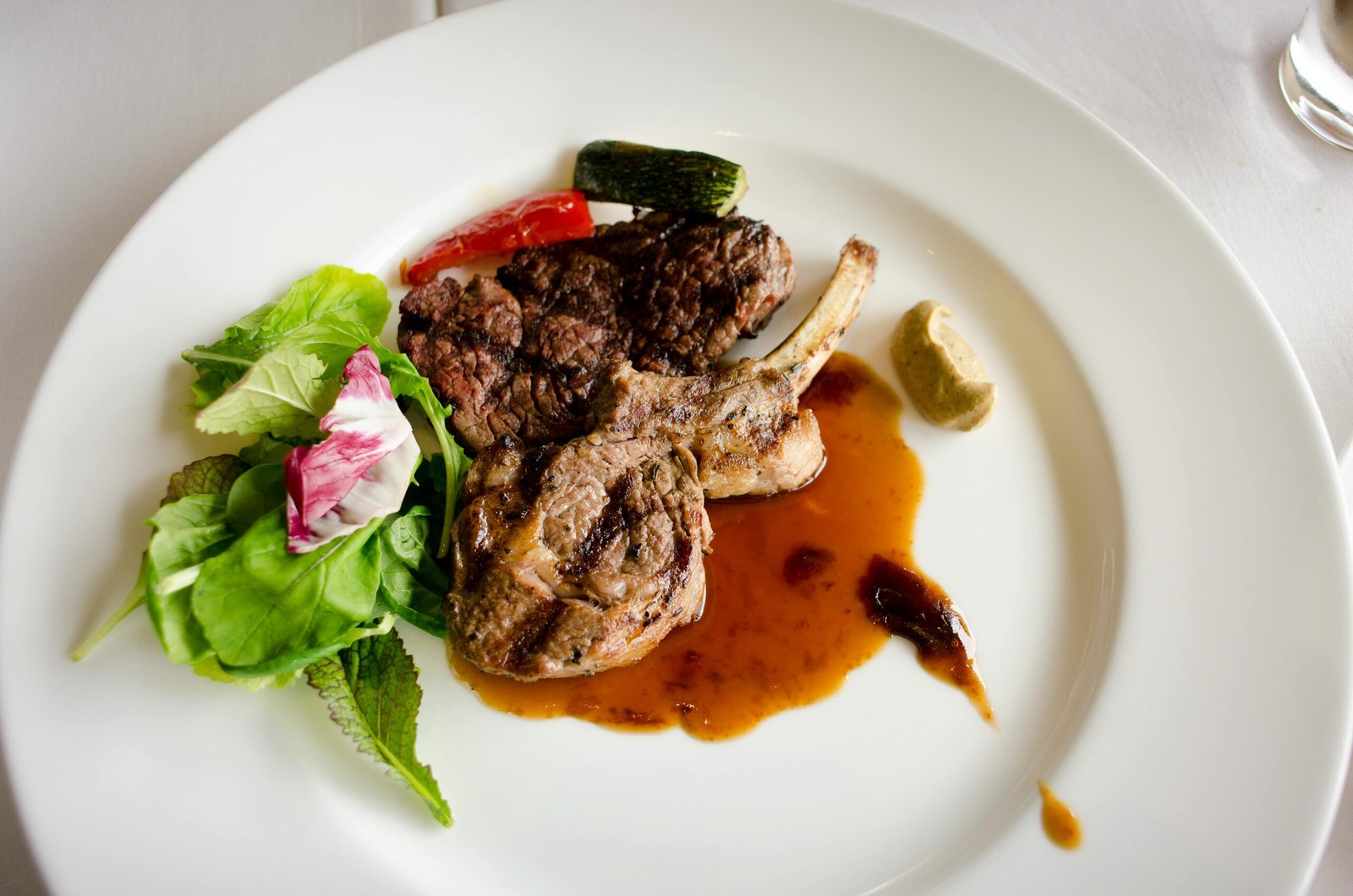 Exquisite lamb chop with sauce, greens and vegetables on a white plate, perfect for fine dining.