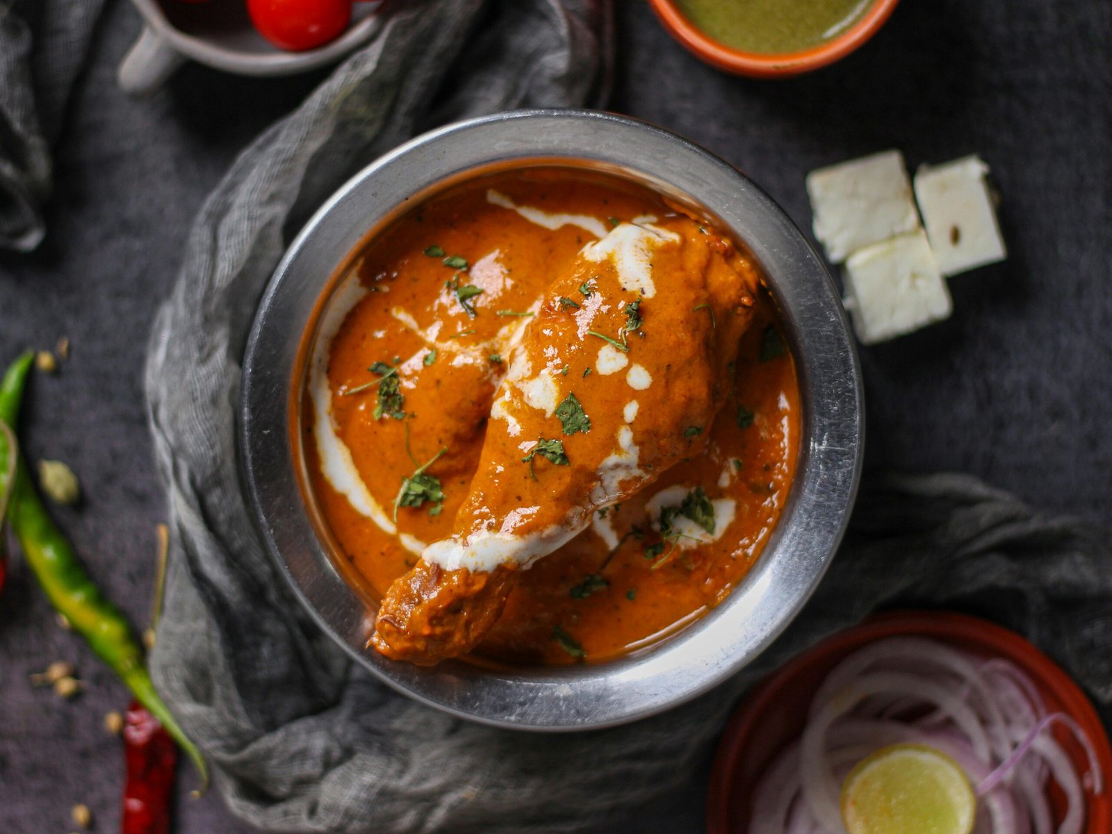 Mouth-watering butter chicken curry garnished with cream and herbs, served in a stainless steel bowl.